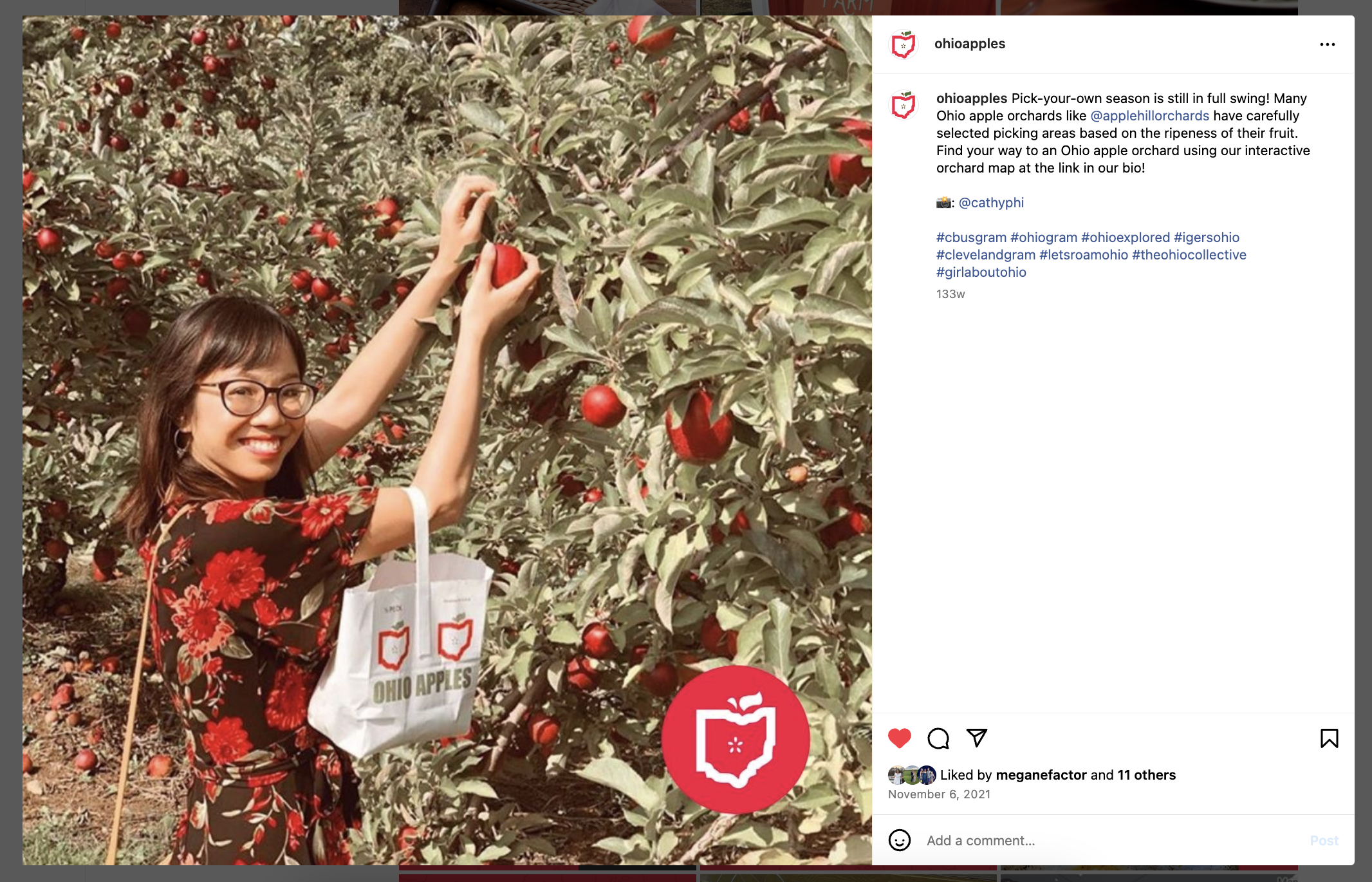 A screenshot of an Instagram post that shows a dark haired woman wearing glasses who is picking apples from a leafy tree.