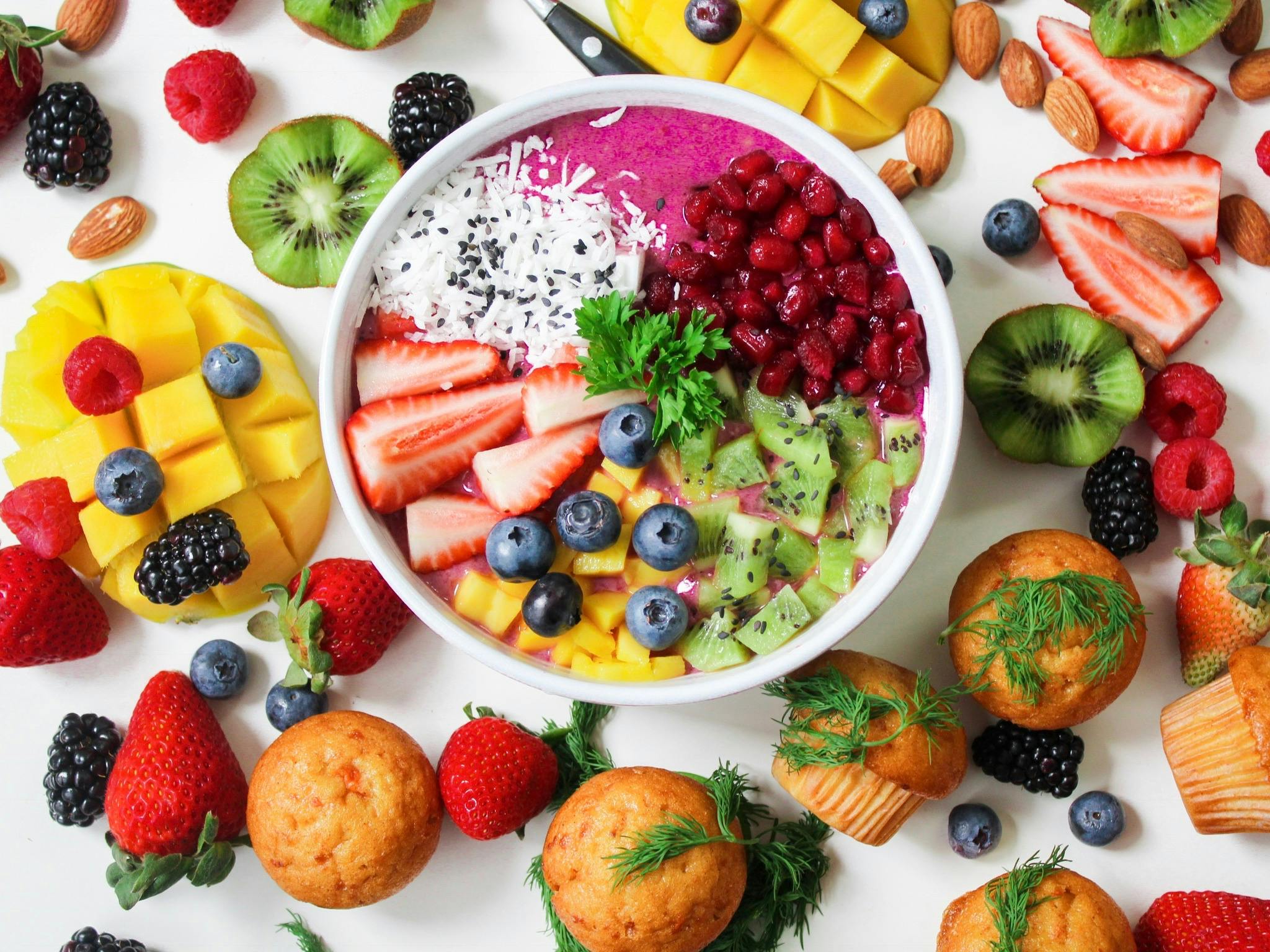 Colorful fruits and muffins spread out on a white table viewed from above